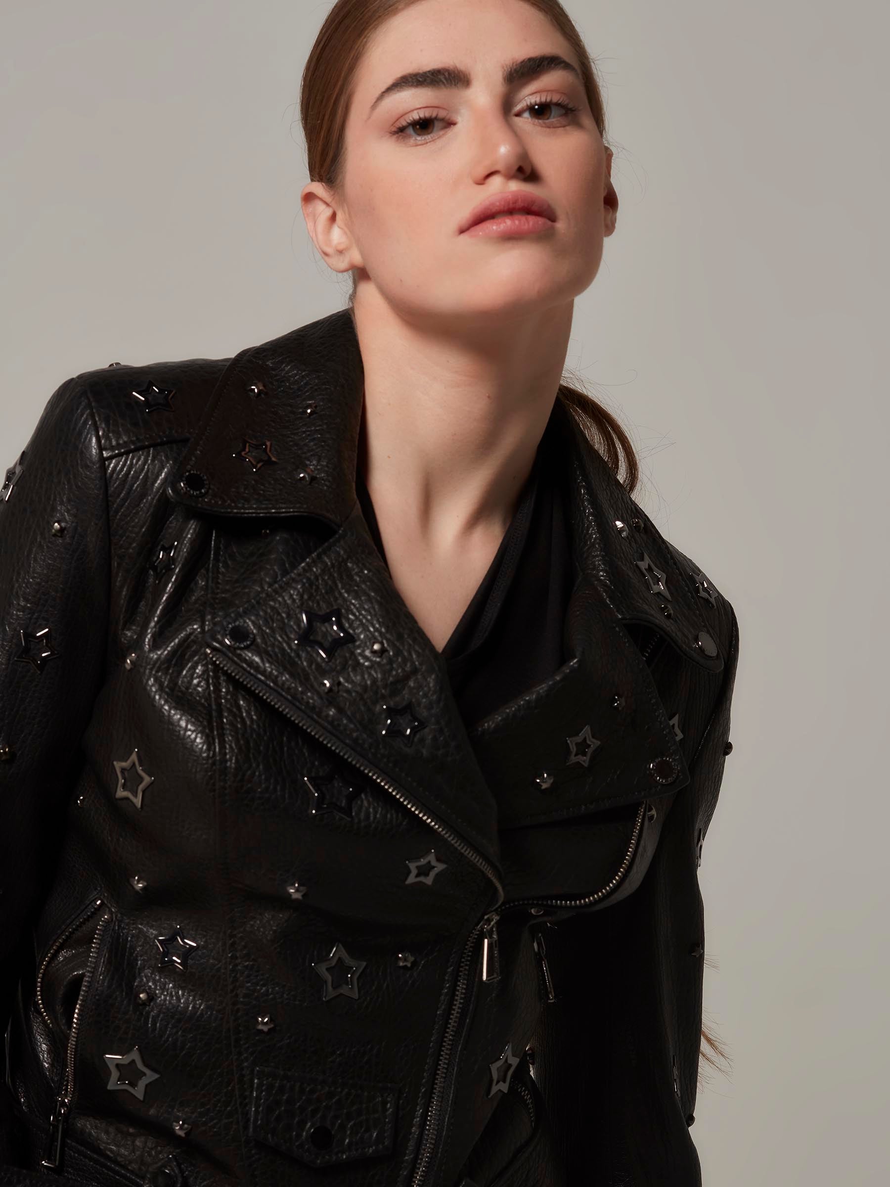 Woman in a black, biker jacket adorned with star details, with the unique texture of the leather and embodying a rebellious rock attitude. Standing side view fashion posing. Motorcycle jacket. Close up.