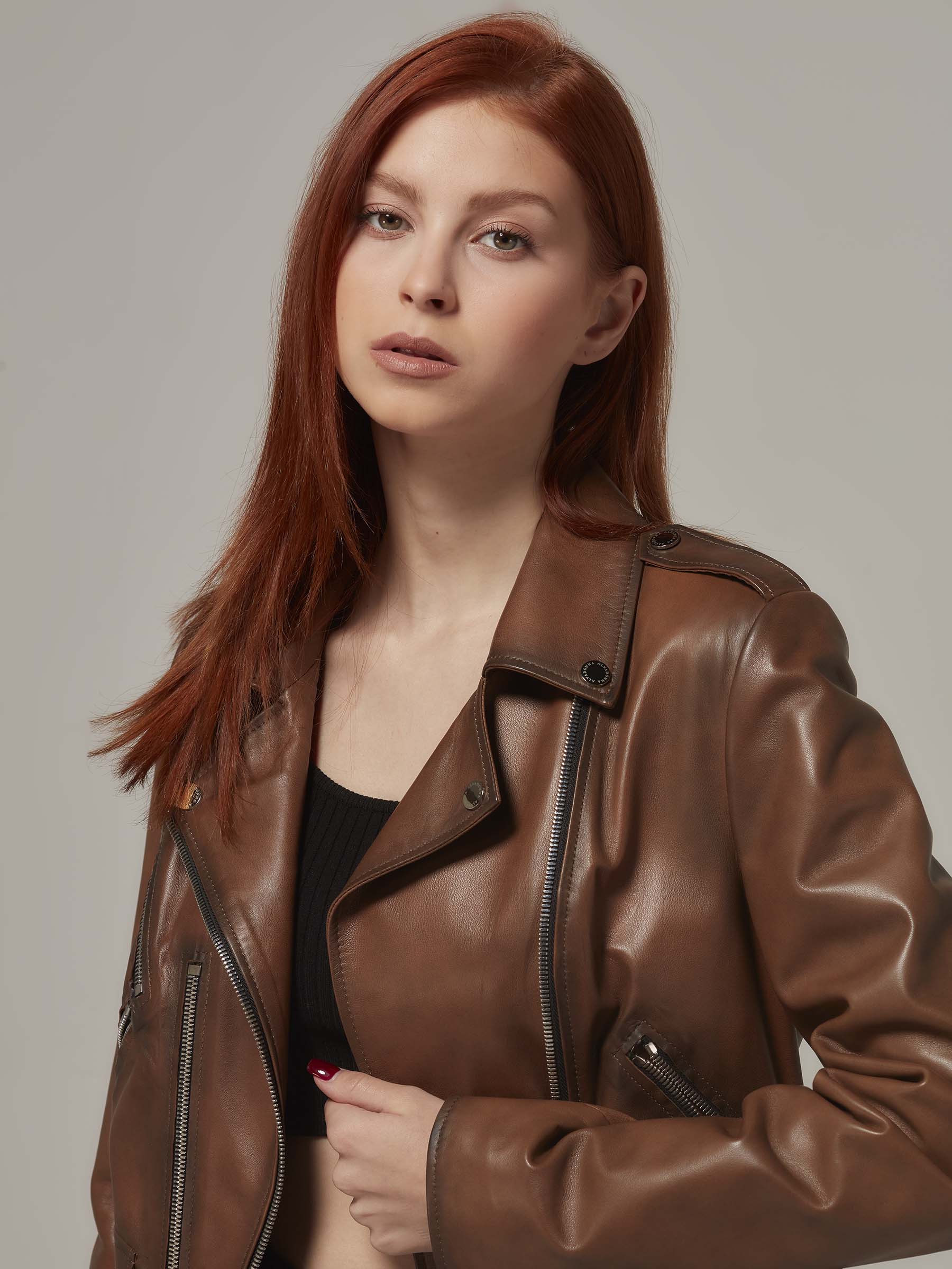 Woman in vintage brown leather biker jacket, motorcycle jacket, moto style, standing. (close up)