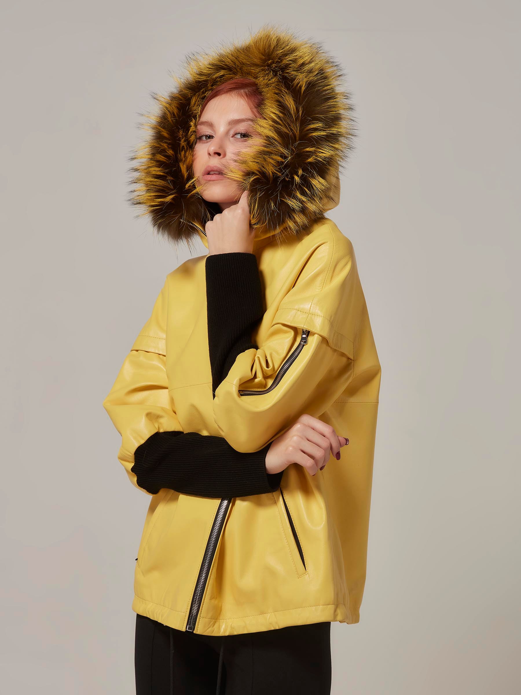 A woman wearing a yellow leather jacket with a black knitted wool sleeve and a fox fur hood.